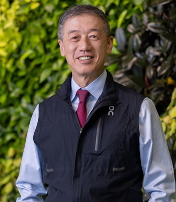 dr gary deng, the director of integrative oncology at the chao family comprehensive cancer center, wearing a vest standing in front of bushes