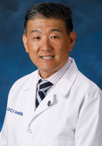 uci health ophthalmologist dr donny suh wearing a white coat in front of a blue studio background