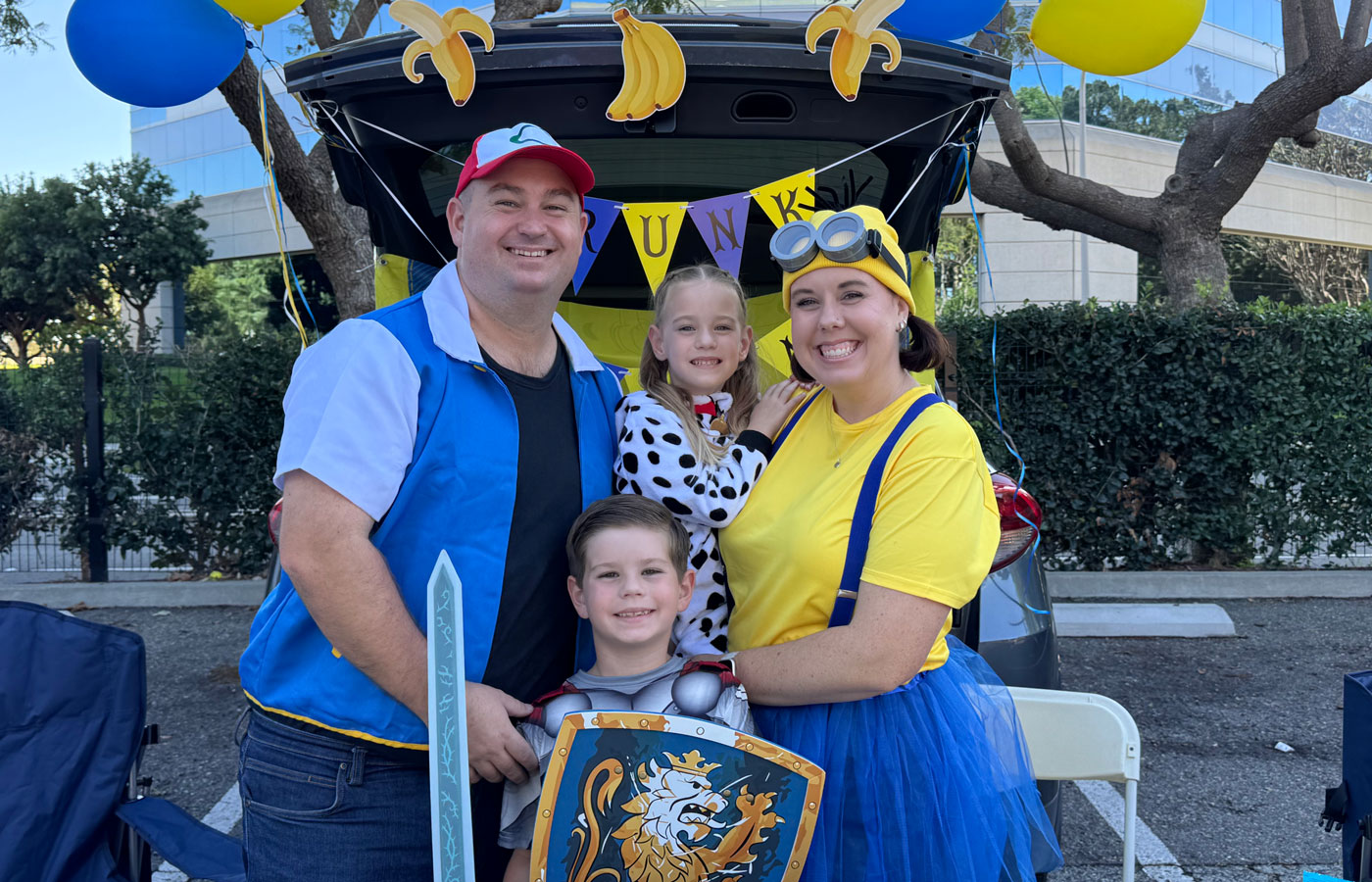 the mckinnon family, two adults and two children, dressed in costume pose for a photo for the NICU reunion carnival outdoors at UCI Health — Orange