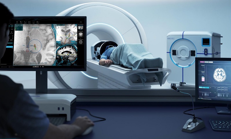 Looking past computer screens in the foreground into an MRI room