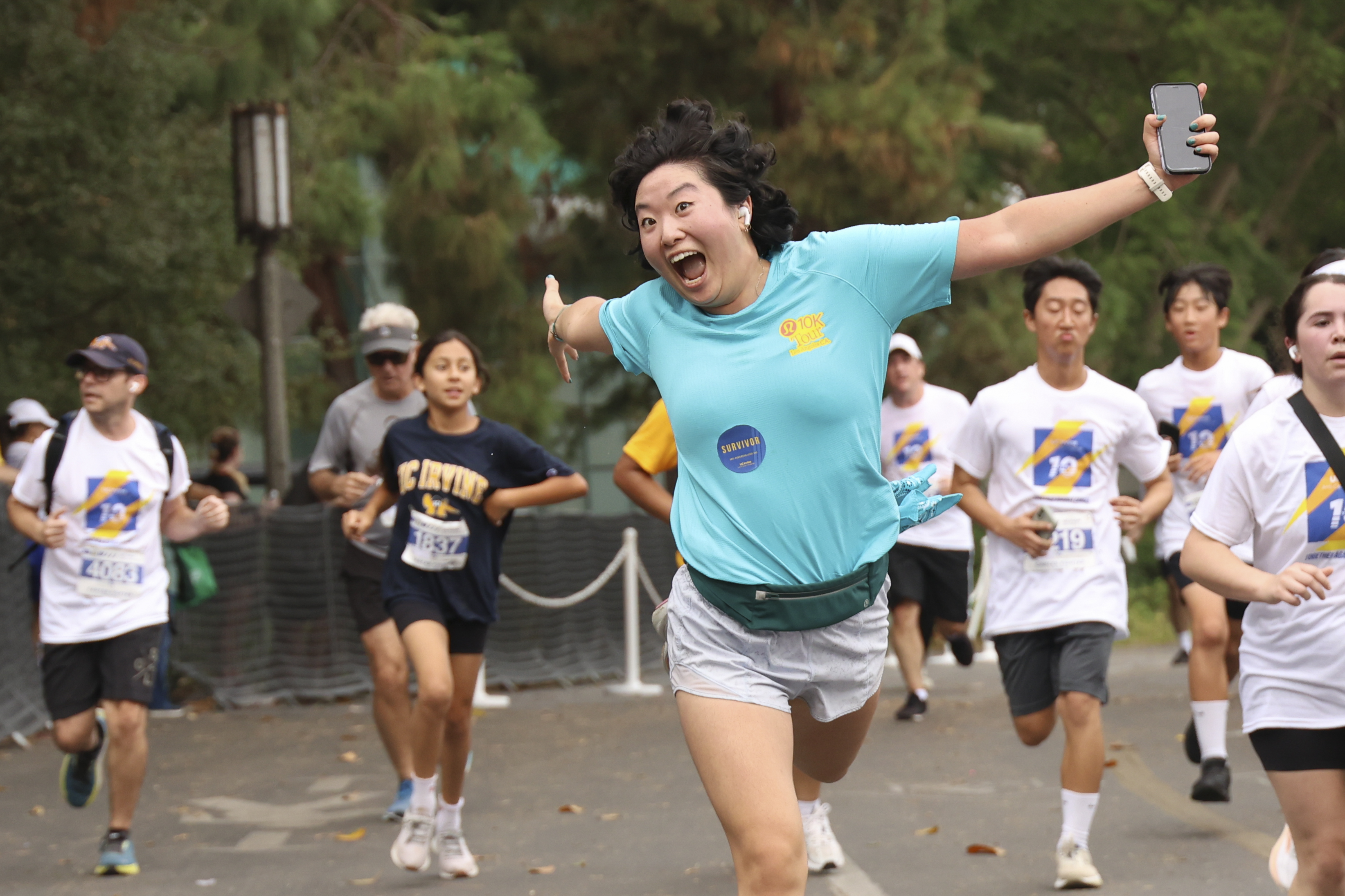 a woman with a big smile wearing an aqua shirt runs during the 2026 uc irvine anti-cancer challenge 