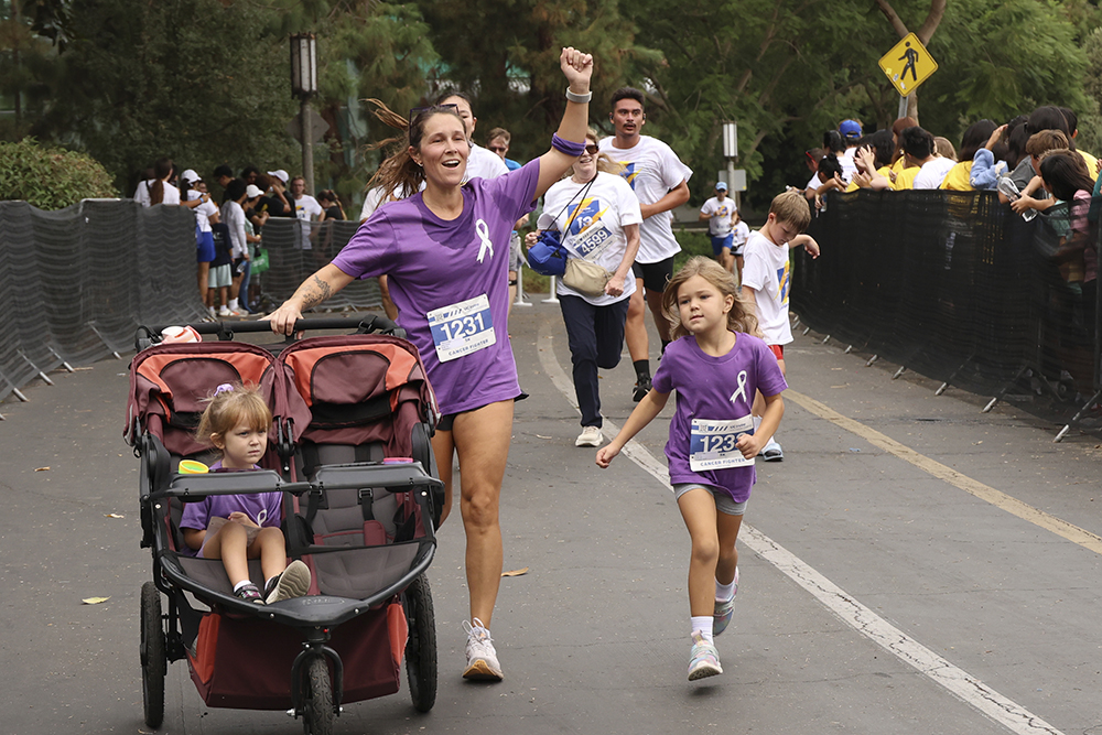 a woman running with her young daughter and children in strollers during the ant-cancer challenge at uc irvine