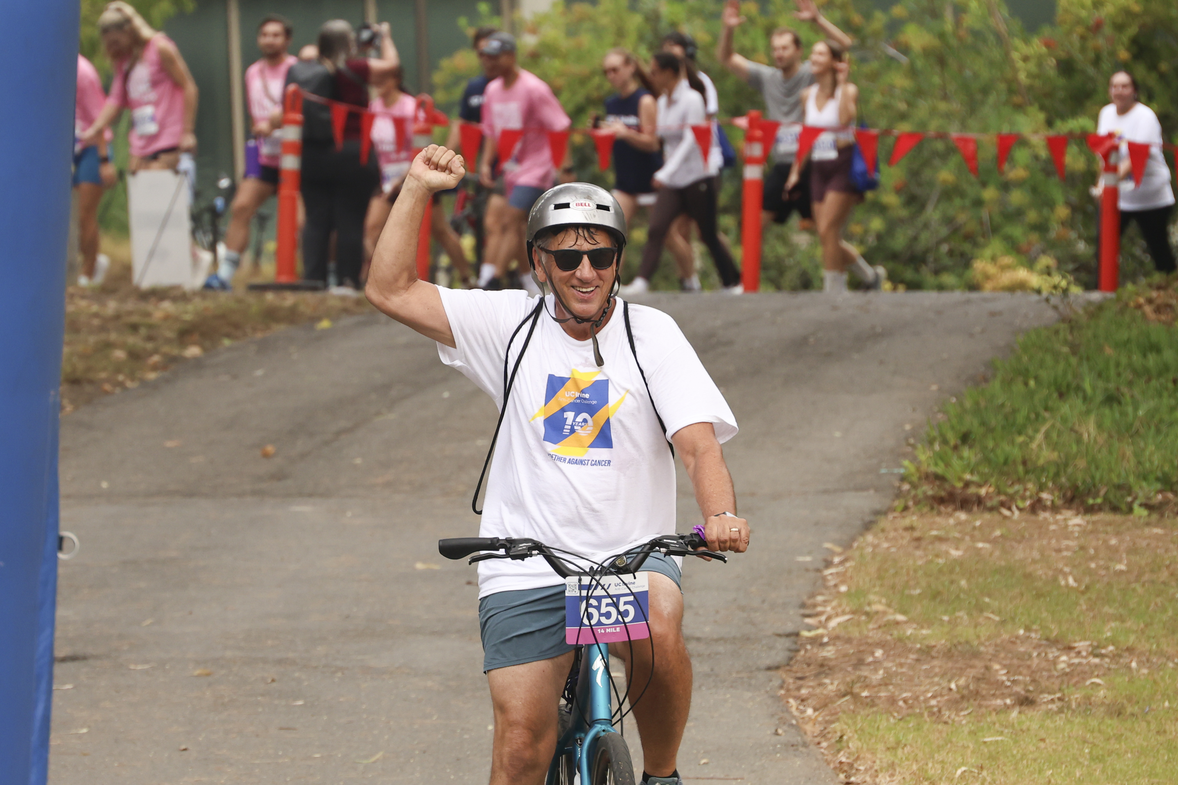 a cyclist wearing a helmet pumps his fist as he rides during the 2026 uc irvine anti-cancer challenge 