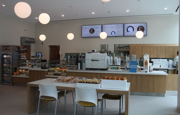 interior shot of the cafe with globe lights, tables, chairs, counter, digital menu and display case at the opening of the tony and daisy fan family cafe at the uci health chao family cancer center and ambulatory care building in Irvine