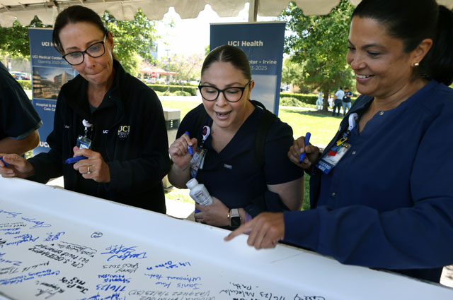 three uci health co-workers smile and sign a white beam covered in signatures before the beam tops off uci health irvine