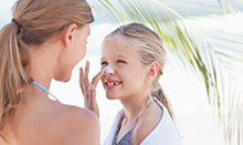 A women applies sunscreen on a young girl at the beach.