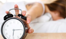 woman in bed snoozing bell alarm clock