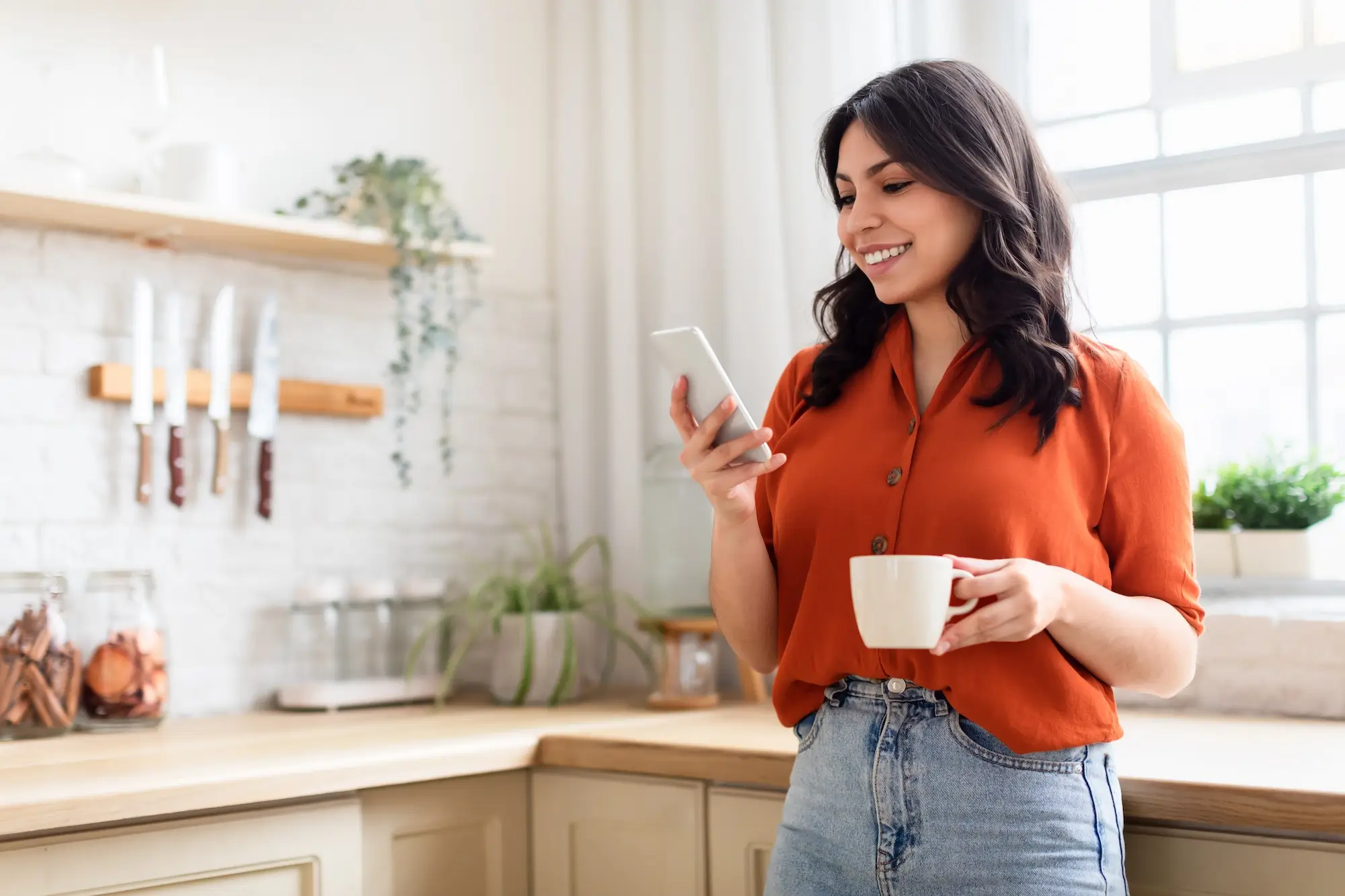 Smiling young woman looks at phone in kitchen