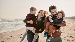 Smiling parents hold two laughing children at the beach in the fall sunshine