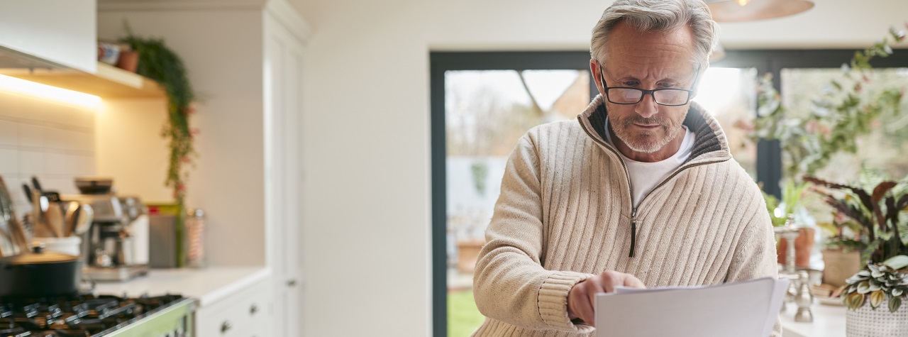 Senior man reviews paperwork in a well-lit kitchen