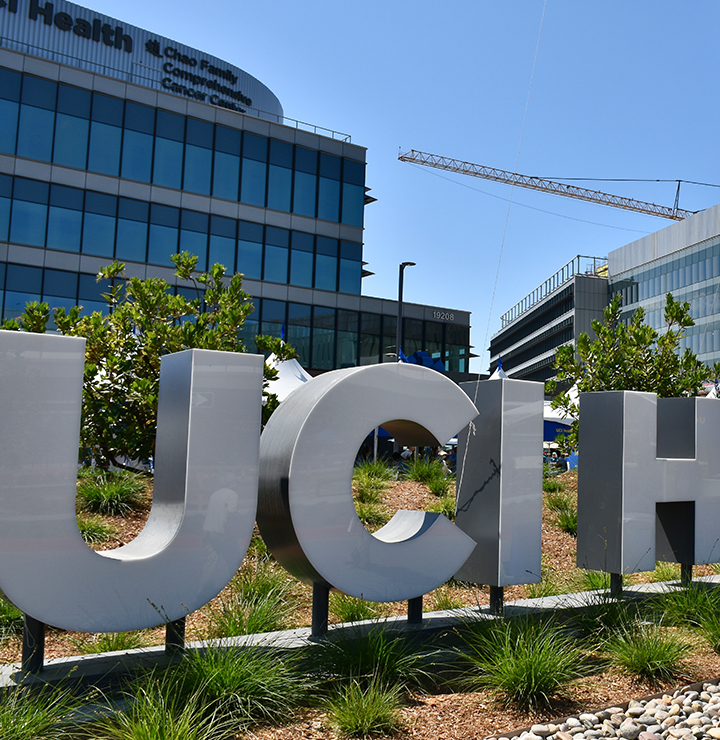 Large "UCI Health" sign in front of modern buildings, surrounded by landscaping with grass and small bushes.