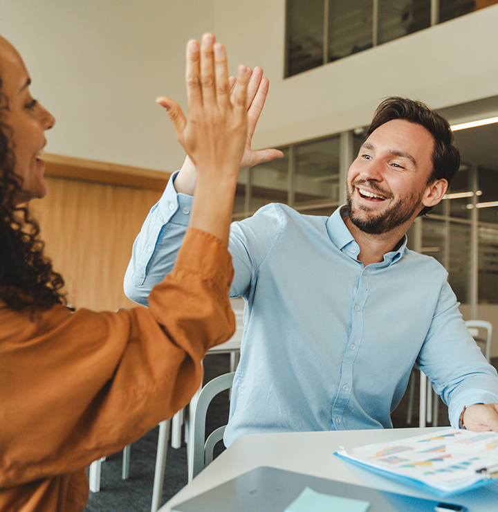 A man and woman smiling as they high-five in an office setting.