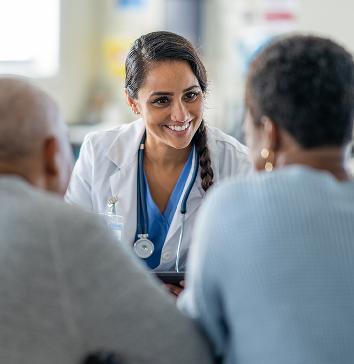 A smiling female doctor wearing a white coat talks to two patients, creating a comforting and reassuring environment in a medical setting.