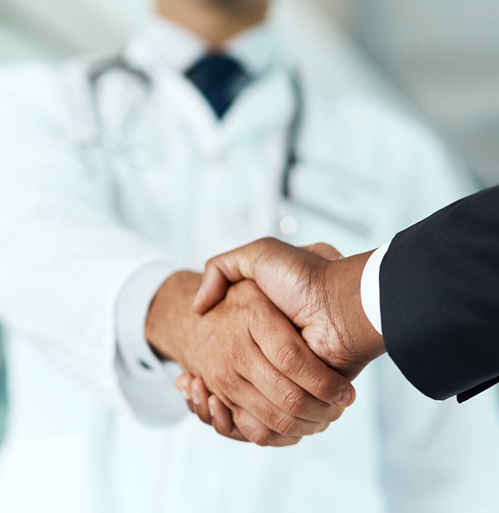 Two people shaking hands; one in a black suit, the other in a white coat, on a blurred background.