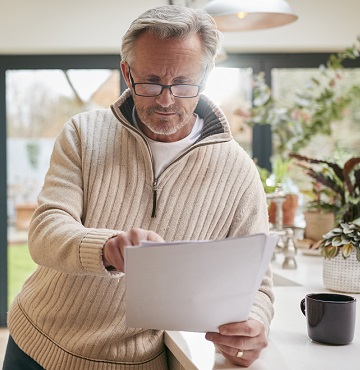 A senior man studies paperwork in a kitchen