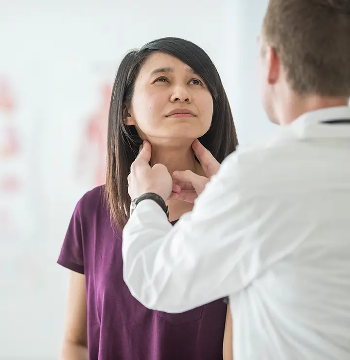 Doctor examines a woman's neck as she looks upward in a medical office.