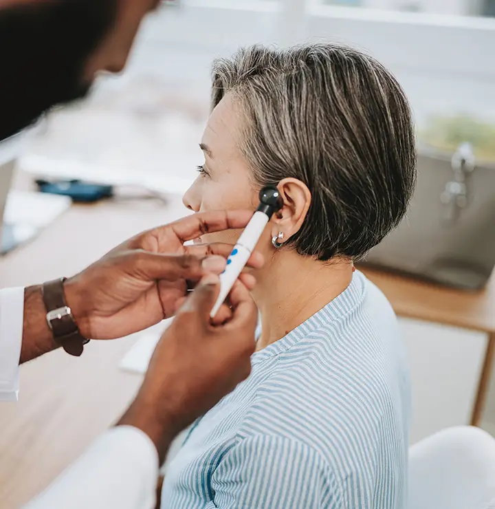 Healthcare professional examines a woman’s ear with an otoscope in a bright office.