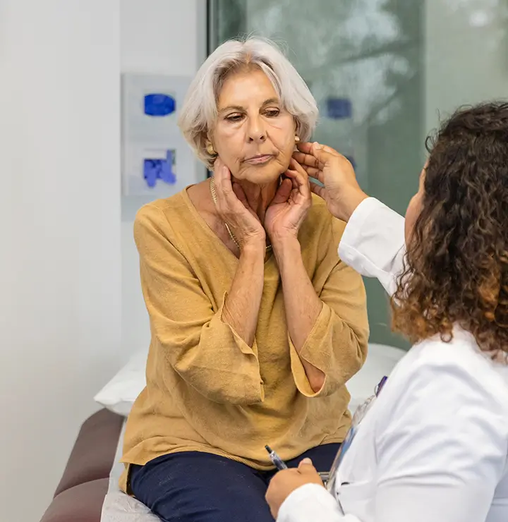 Doctor examines a woman’s jawline in a bright medical office with large windows.