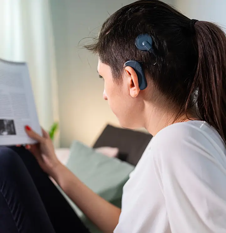 Person with short hair reading a magazine while wearing a cochlear implant.