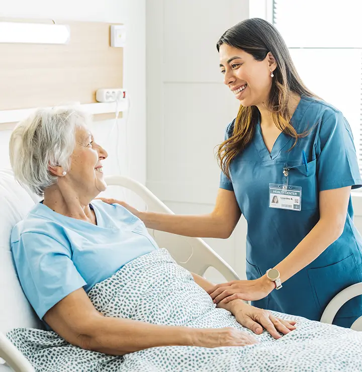 Nurse comforts an elderly woman in a hospital bed with a supportive smile.