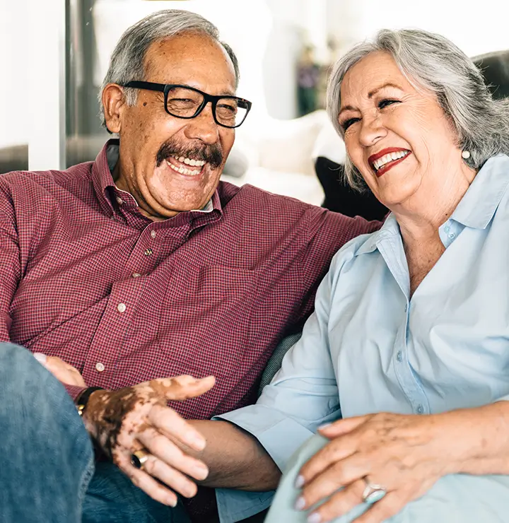 Elderly couple laughing joyfully on a sofa, sharing a happy moment.