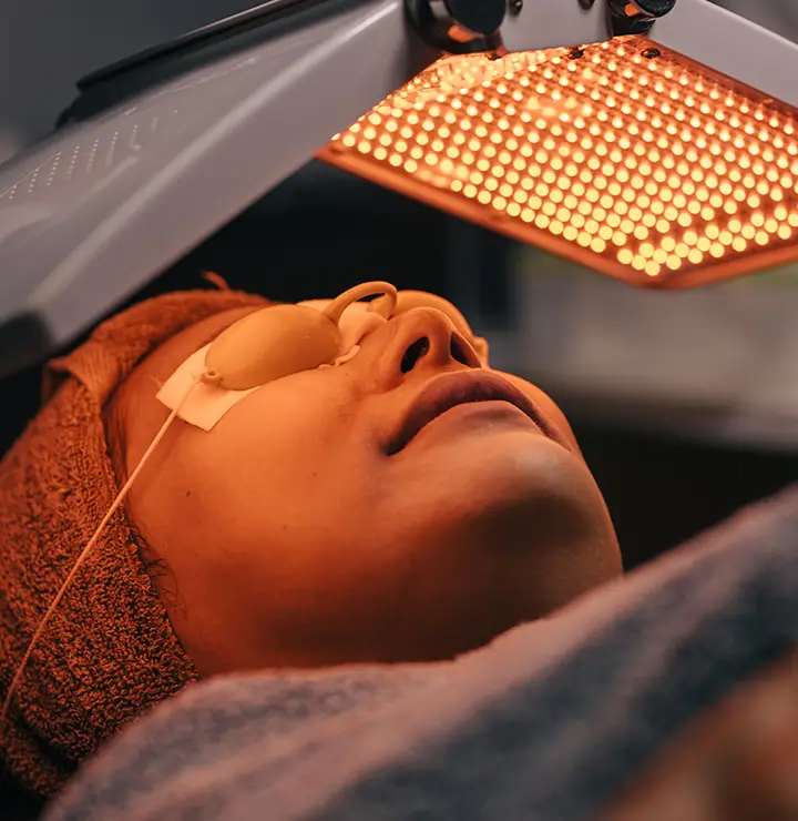 Person lying under LED light therapy device, wearing protective eyewear.