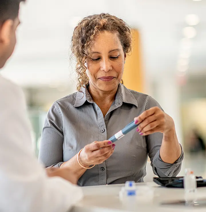 Woman holding a device for a blood sugar test while sitting at a table.