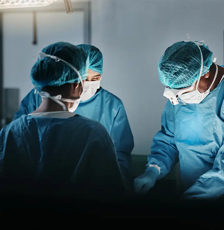 Three surgeons focus on a procedure under bright lights, wearing gowns, masks, and caps.