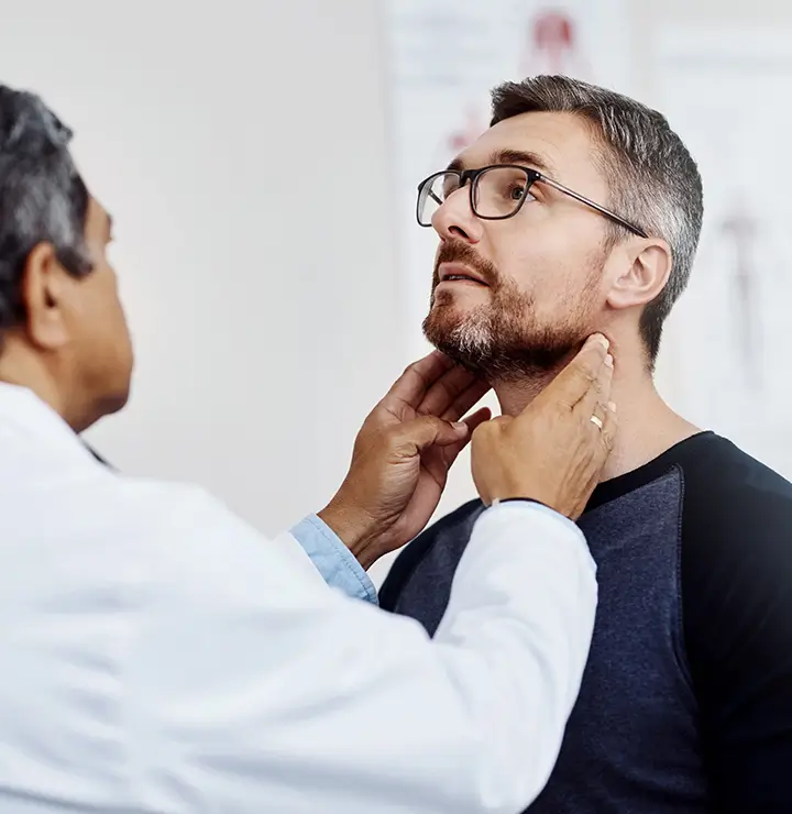 Doctor examines a man's neck, pressing under his jaw in a medical office.