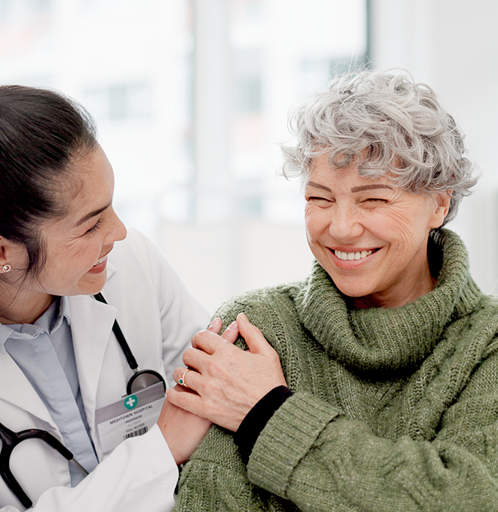 the doctor compassionately places a hand on the patients shoulder as they both smile at each other