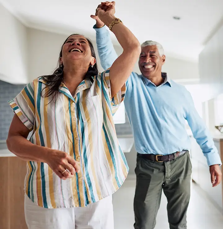 A cheerful couple dances in their kitchen, smiling warmly and creating a happy, vibrant atmosphere.