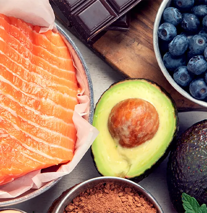 Close-up of healthy foods: raw salmon, avocado, blueberries, chocolate, and cocoa powder.