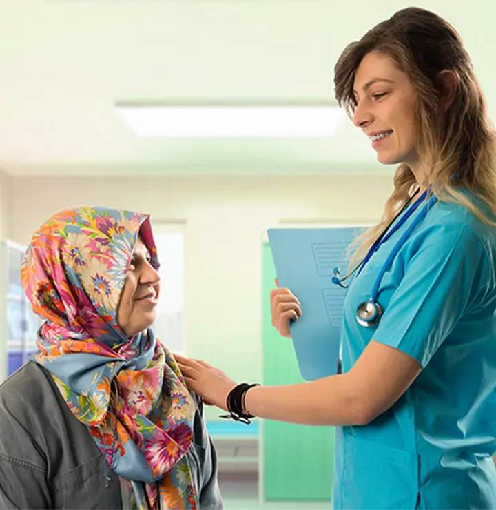 Healthcare worker places a supportive hand on an older woman in a floral scarf.