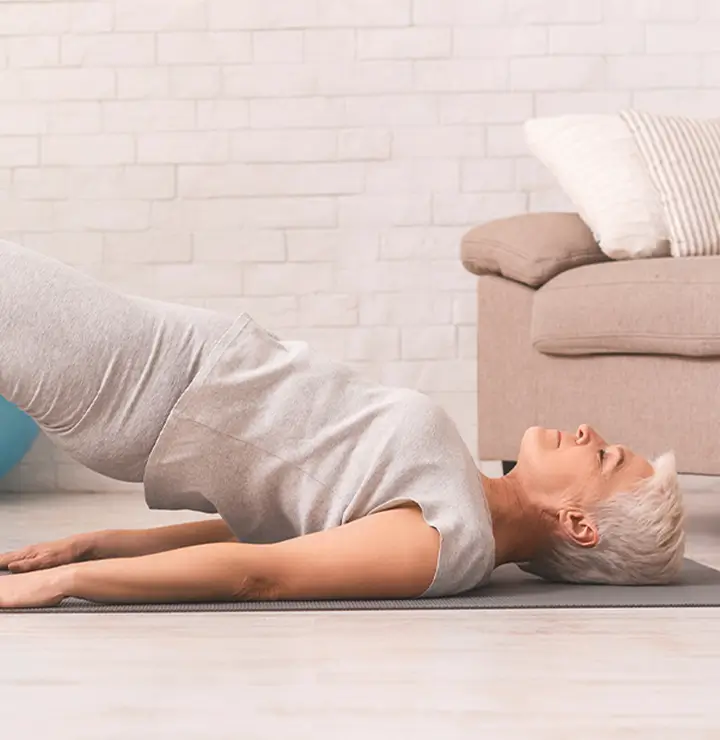 Person in gray outfit performs a bridge pose indoors near a white wall.