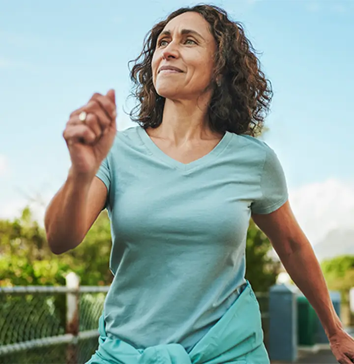 Woman enjoys an outdoor walk wearing a light blue shirt and jacket tied at her waist.