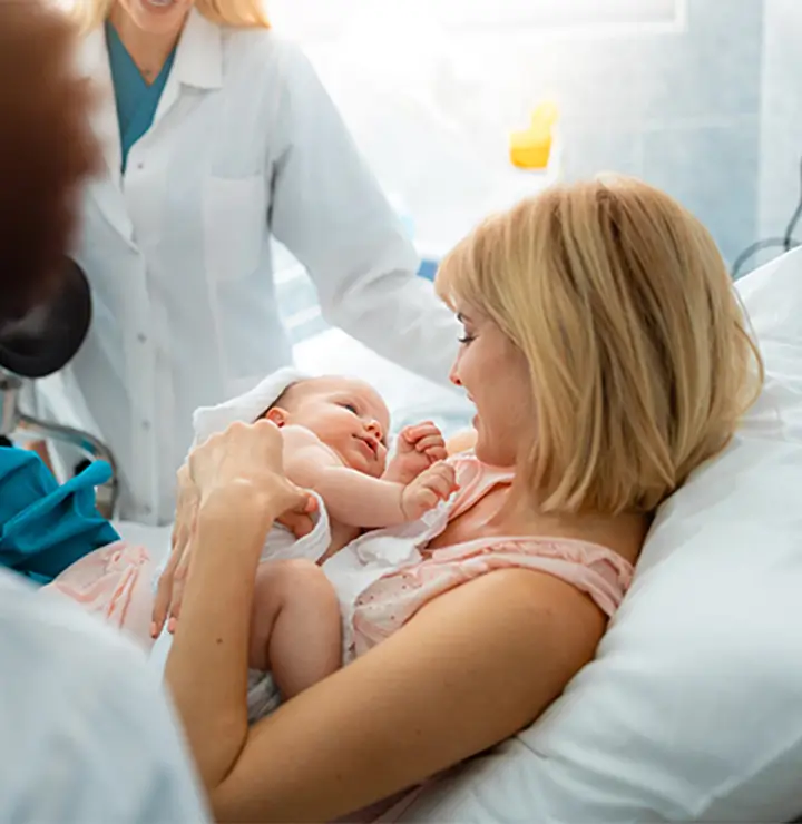 Mother smiles in a hospital bed, holding her newborn in a warm moment.