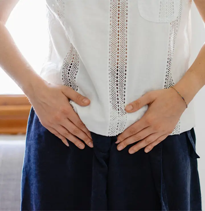 Person in lace-accented top and dark pants stands indoors with hands on hips.