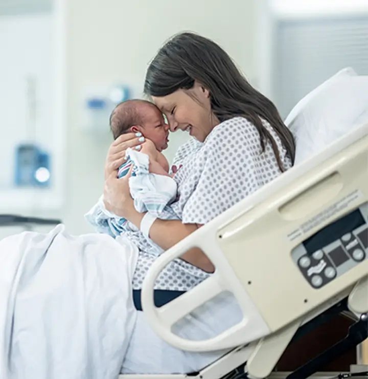 Mother and newborn touch foreheads in a softly lit hospital room.