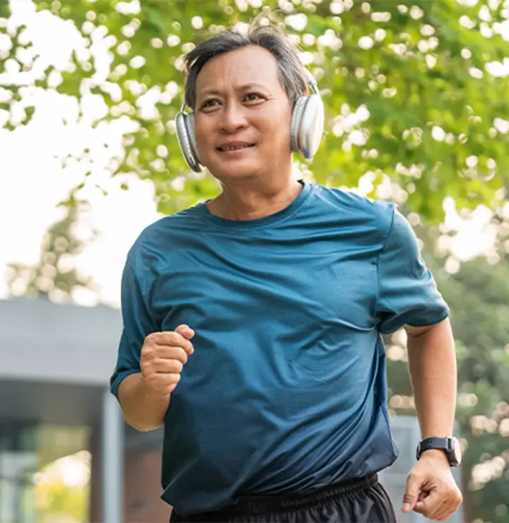 Man jogging outdoors in a blue shirt and headphones under sunny skies.