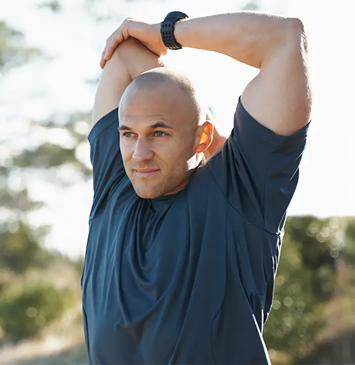 Man stretches arms overhead outdoors in a sunny setting.