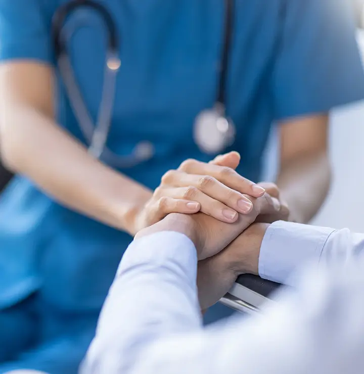 Healthcare worker holds another’s hands in a supportive medical setting.