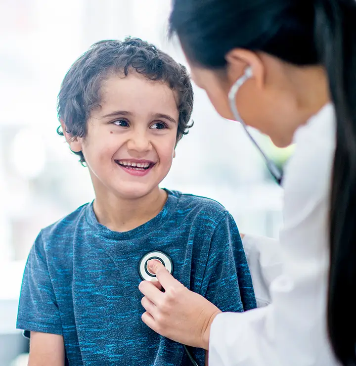 Boy smiles as a healthcare worker listens to his heartbeat with a stethoscope.