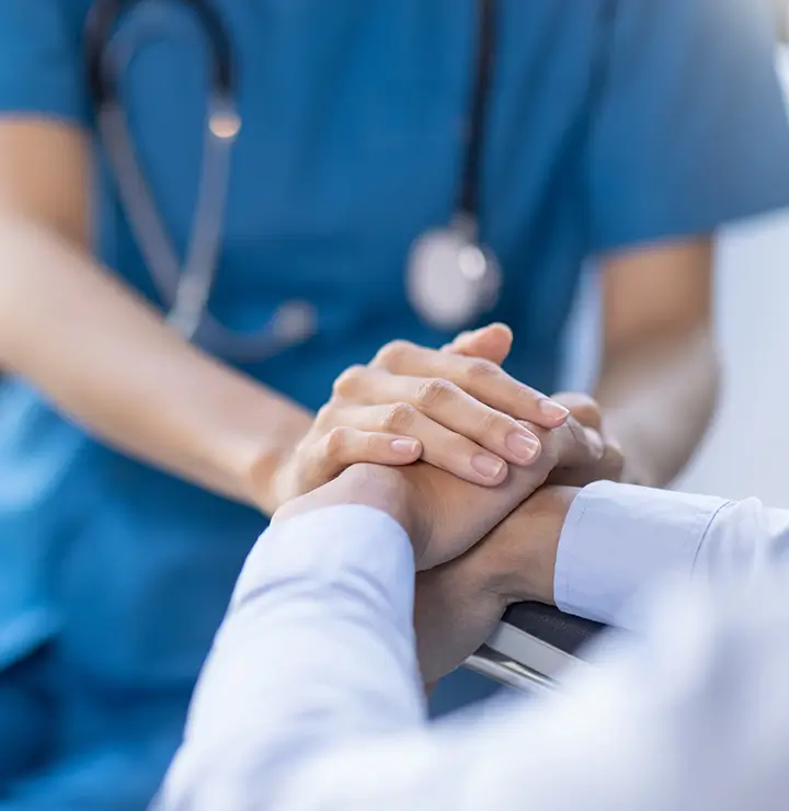 A nurse comforting a patient by holding their hands in a hospital setting.