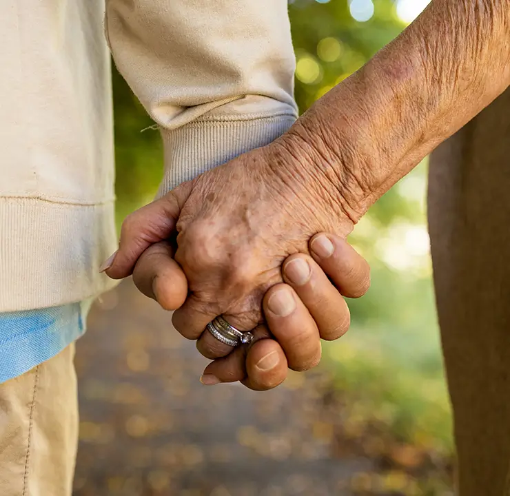 Two people holding hands, one wearing a ring. The focus is on their hands, with a blurred background.