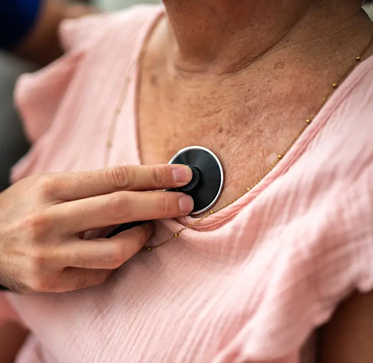A person using a stethoscope to listen to a patient's heartbeat on their chest.