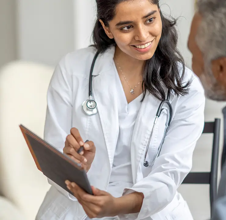 A doctor with a stethoscope smiles while speaking to an older man in a medical office setting.