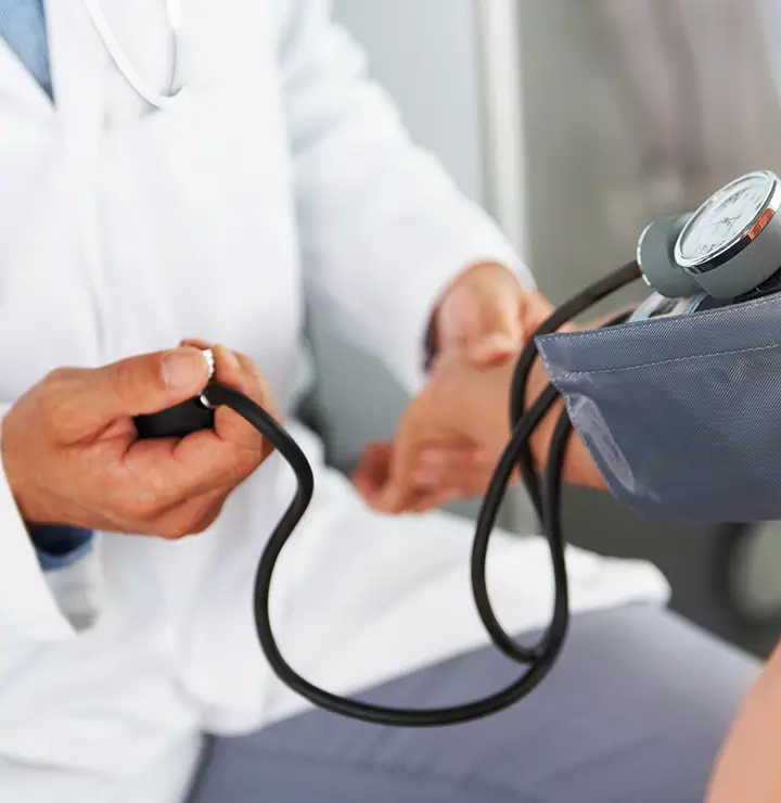 A doctor checks a patient's blood pressure using a sphygmomanometer and stethoscope.