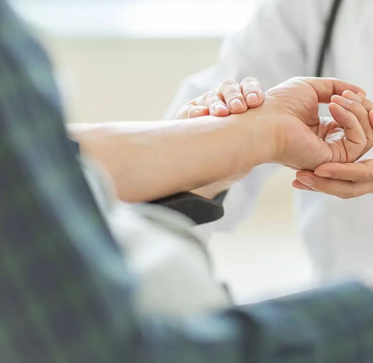 A doctor in a white coat checking a patient's pulse on their wrist with a stethoscope around the neck.