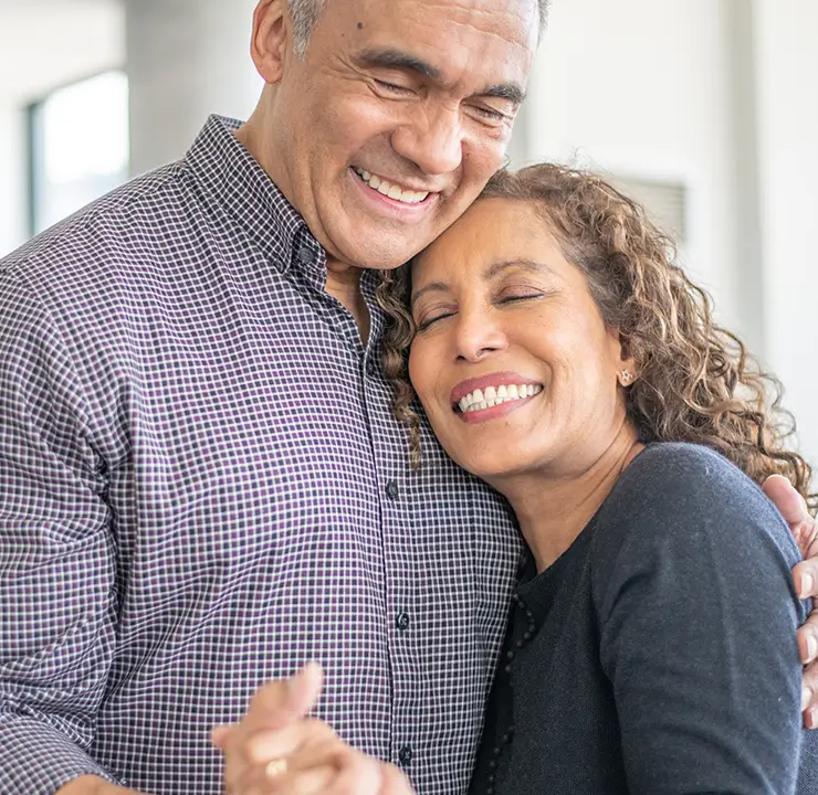A smiling couple embraces warmly in a bright living room.
