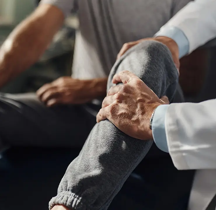 A doctor examines a patient's knee, both in casual attire, in a medical office.